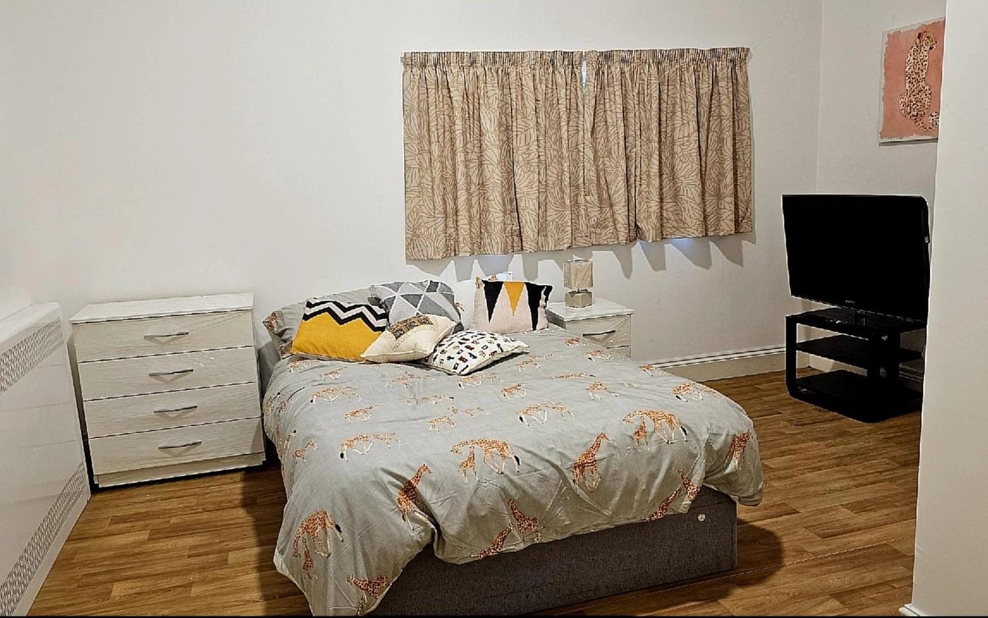 A furnished bedroom with wardrobe, chest of drawers and television