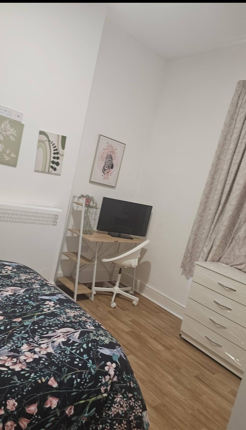 A furnished bedroom with a study desk, chair and television
