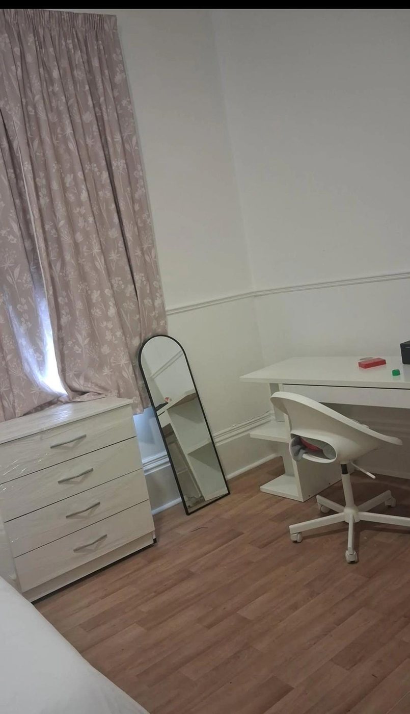 A furnished bedroom with a desk, chair and full-length mirror